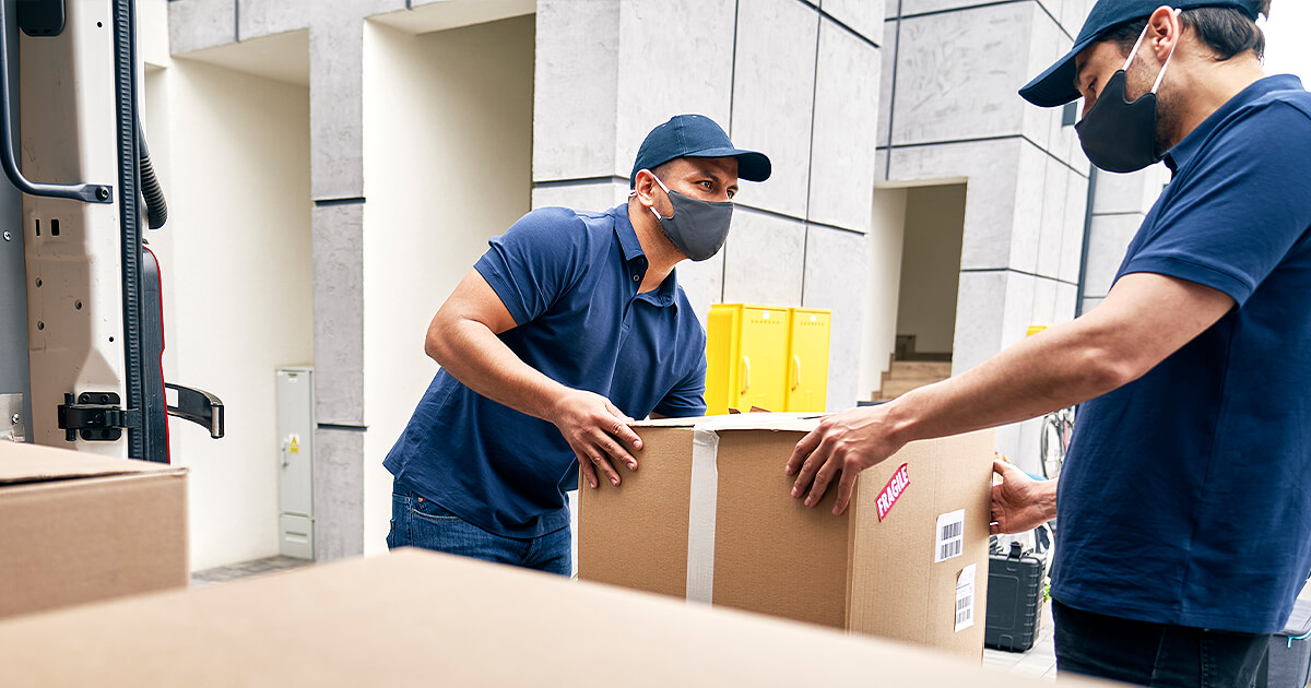 Two interstate removalists with face masks unload boxes from moving truck