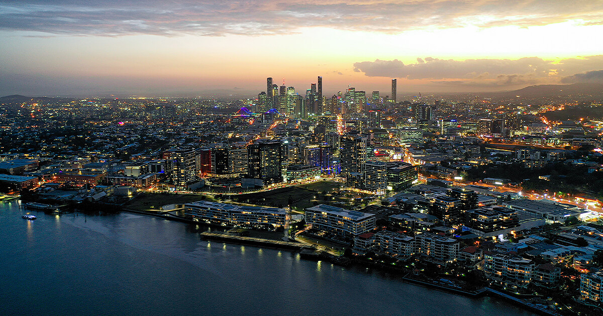 Aerial view of Brisbane lit up at dusk with sun setting in background