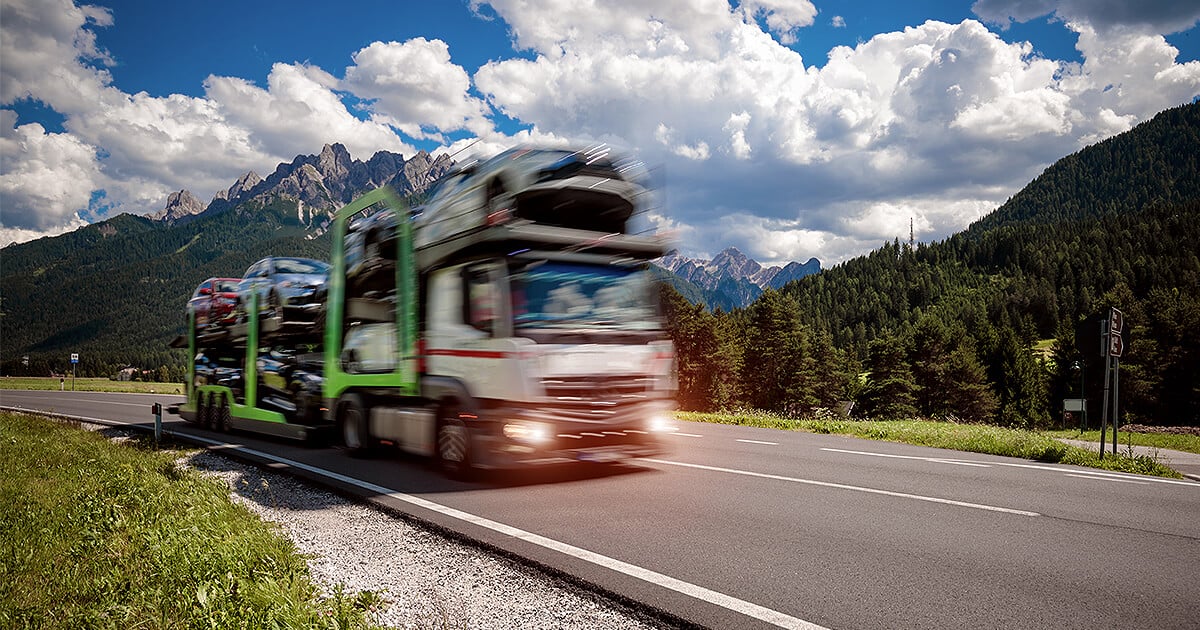 Interstate car transport truck driving through green mountain range