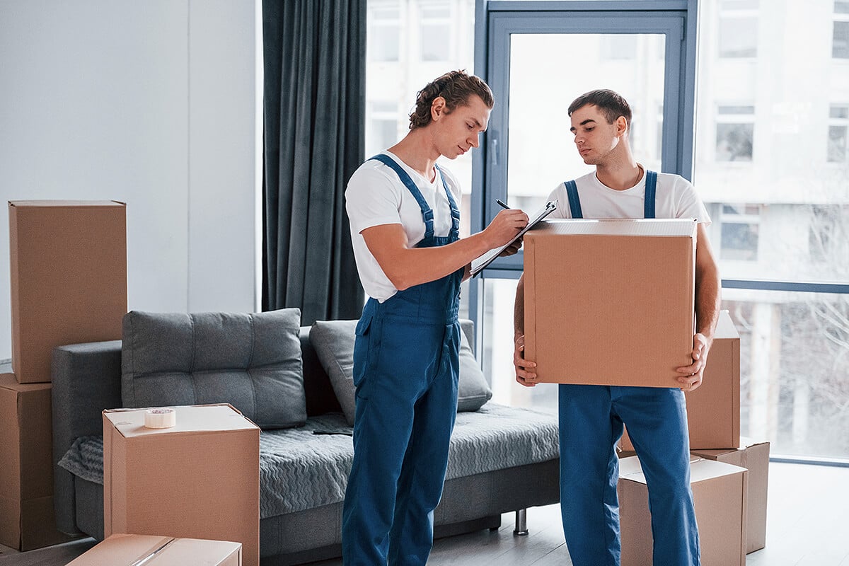 Two removalists filling out paperwork while moving boxes