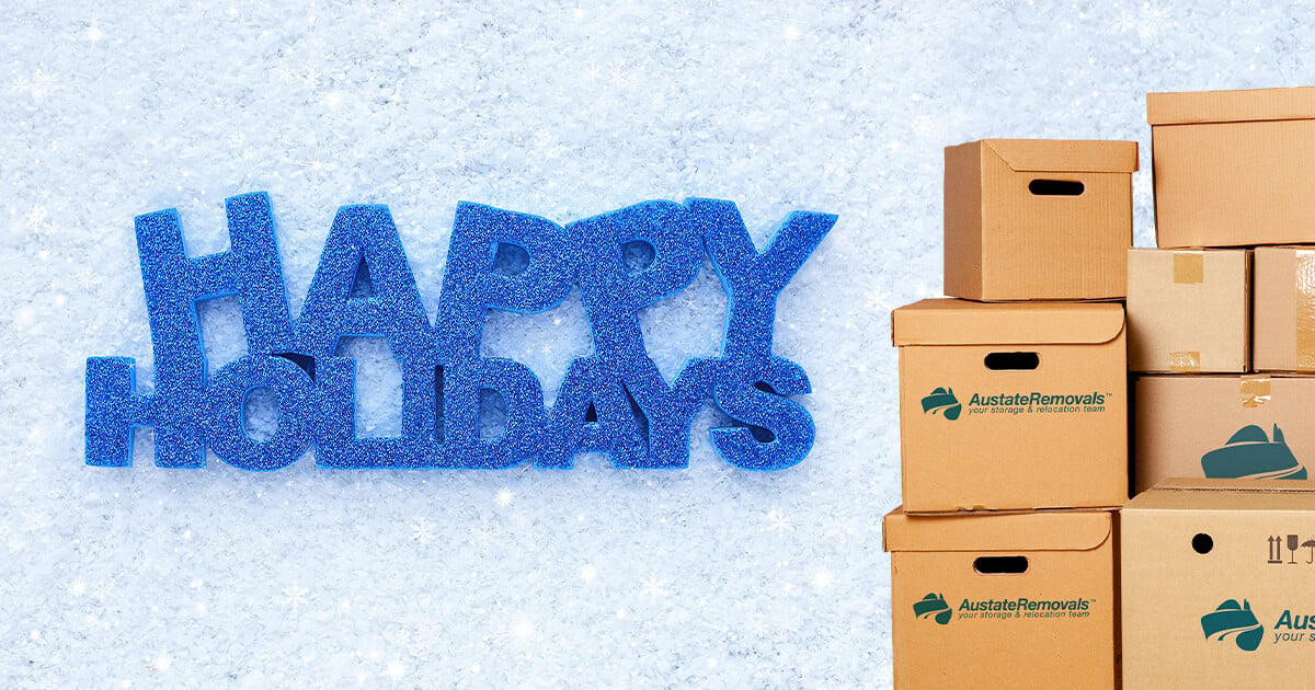 Blue glitter "Happy Holidays" text on snow background with stack of boxes on right.
