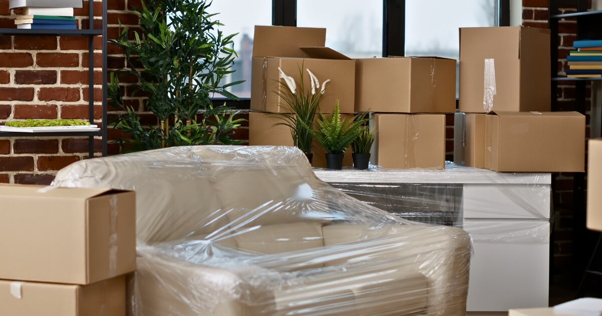 Couch wrapped in plastic with moving boxes in the background