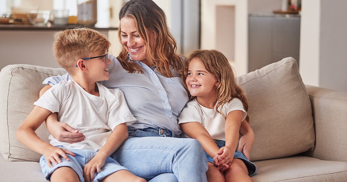 Mother and two children sit on couch talking in rental