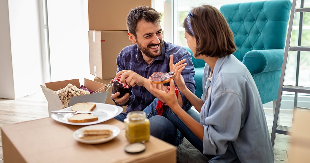 Middle aged couple sitting eating breakfast on moving boxes during moving day