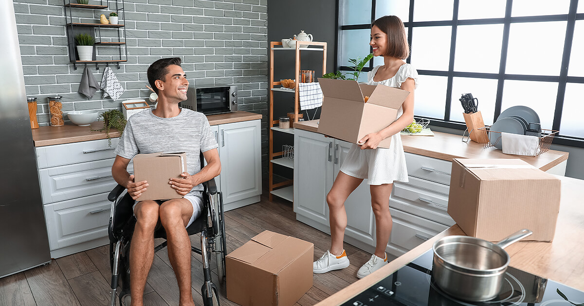 Young couple with man in wheelchair pack boxes in kitchen for move