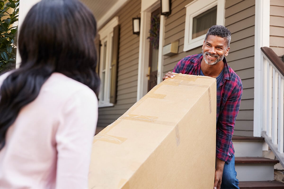 Couple move tv in large box down stairs ready to be moved