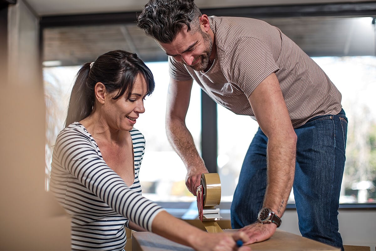 Man and woman tape down packing box full of home items