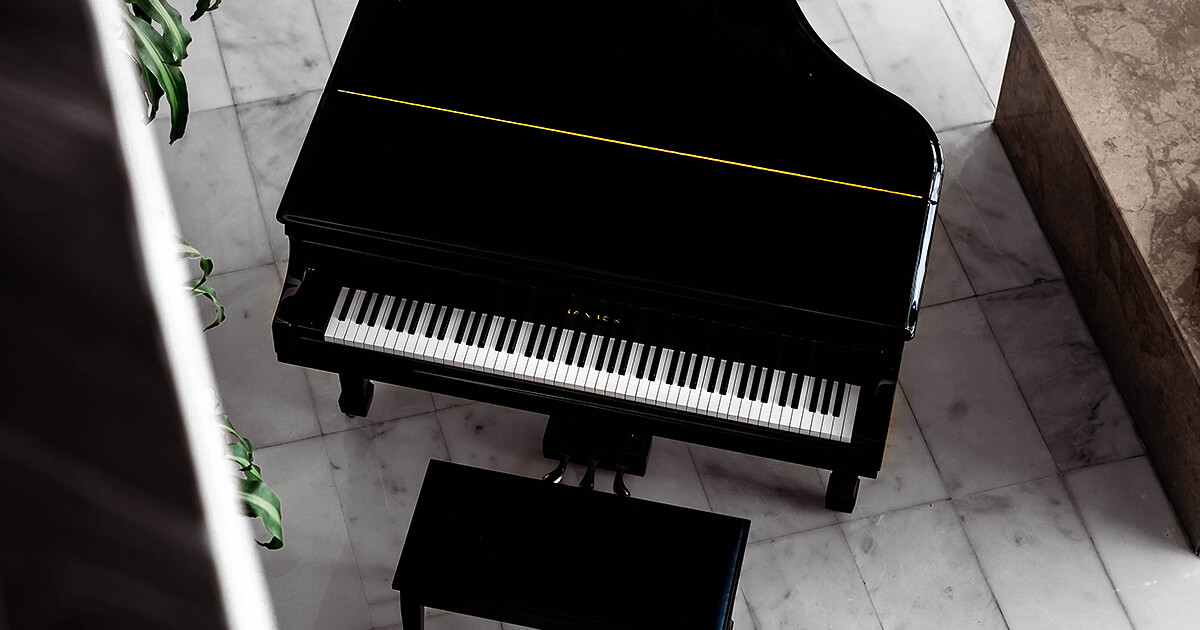 Large black grand piano and stool set up on tiles on bottom floor of building