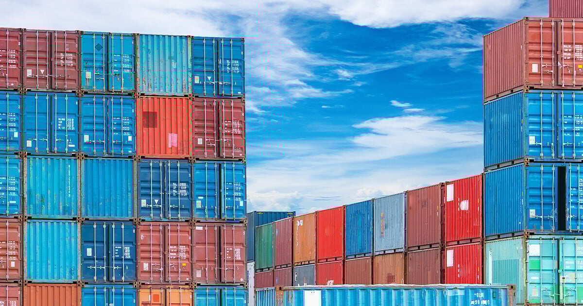 Shipping containers stacked on each other in port with blue cloudy sky behind
