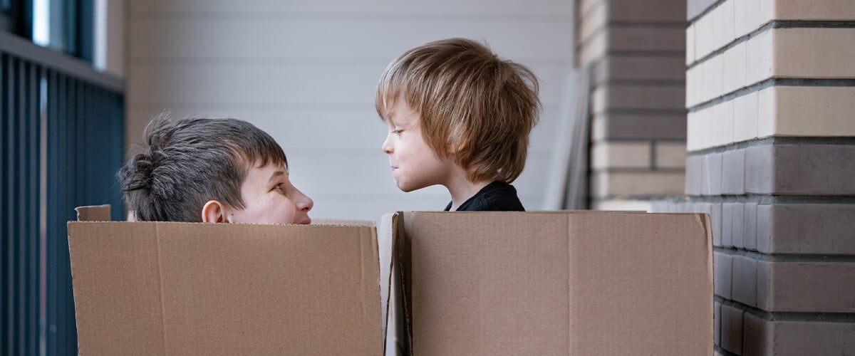 Two young kids sitting in boxes playing waiting for their interstate move